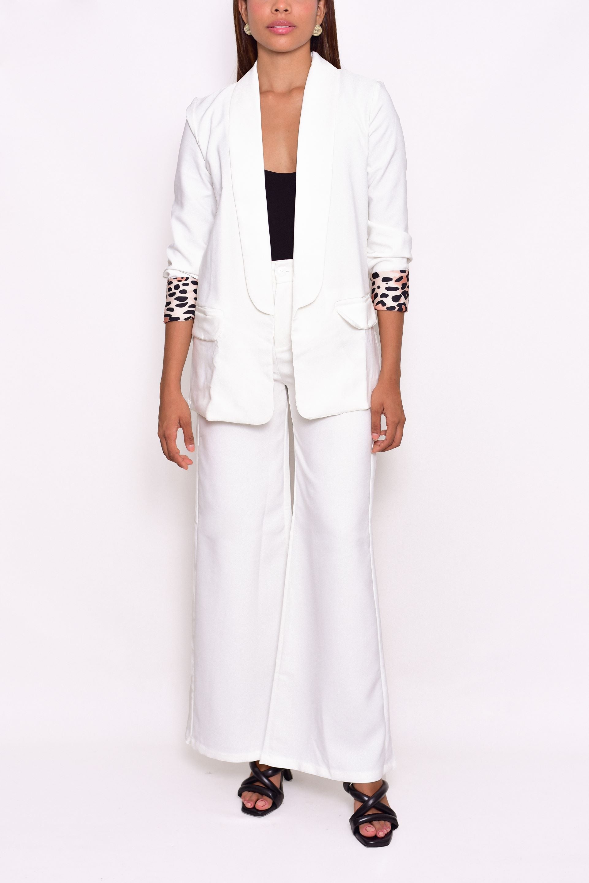 Conjunto blanco de blazer y pantalón palazzo, confeccionado en Colombia. El blazer de corte recto presenta solapas anchas y detalles de puños con estampado animal print, combinando elegancia y un toque audaz. El pantalón de tiro alto y pierna ancha estiliza la silueta. Ideal para un look sofisticado y moderno.