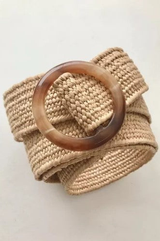Cinturón tejido en fibra natural con hebilla circular en tonos marrón y beige. Diseño artesanal, versátil y ajustable, ideal para complementar looks casuales o bohemios con un toque elegante y natural.