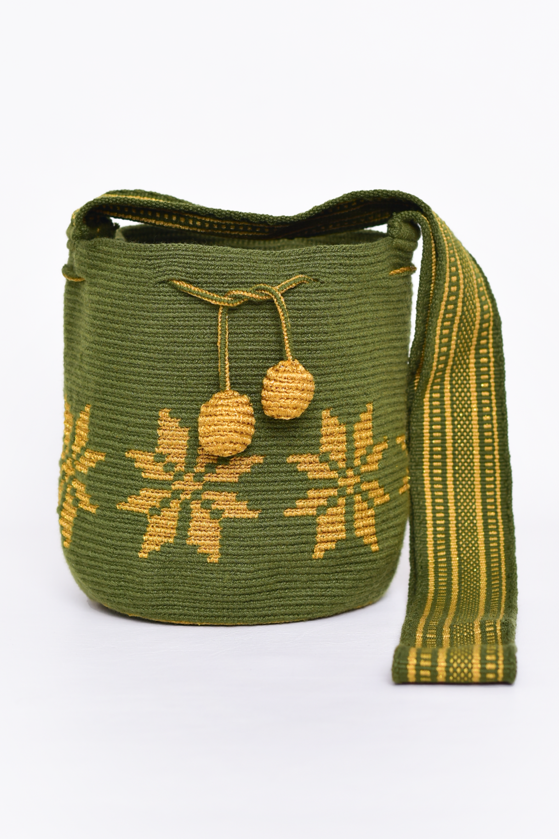 Mochila artesanal Wayuu 100% hecha a mano con hilos de algodón y seda dorada, diseñada por artesanas indígenas de la Comunidad Wayuu. Presenta un diseño de flores en tonos dorados, un asa larga, cordón ajustable y borlas decorativas, todo en color blanco. Un accesorio único que refleja la riqueza de la moda colombiana.