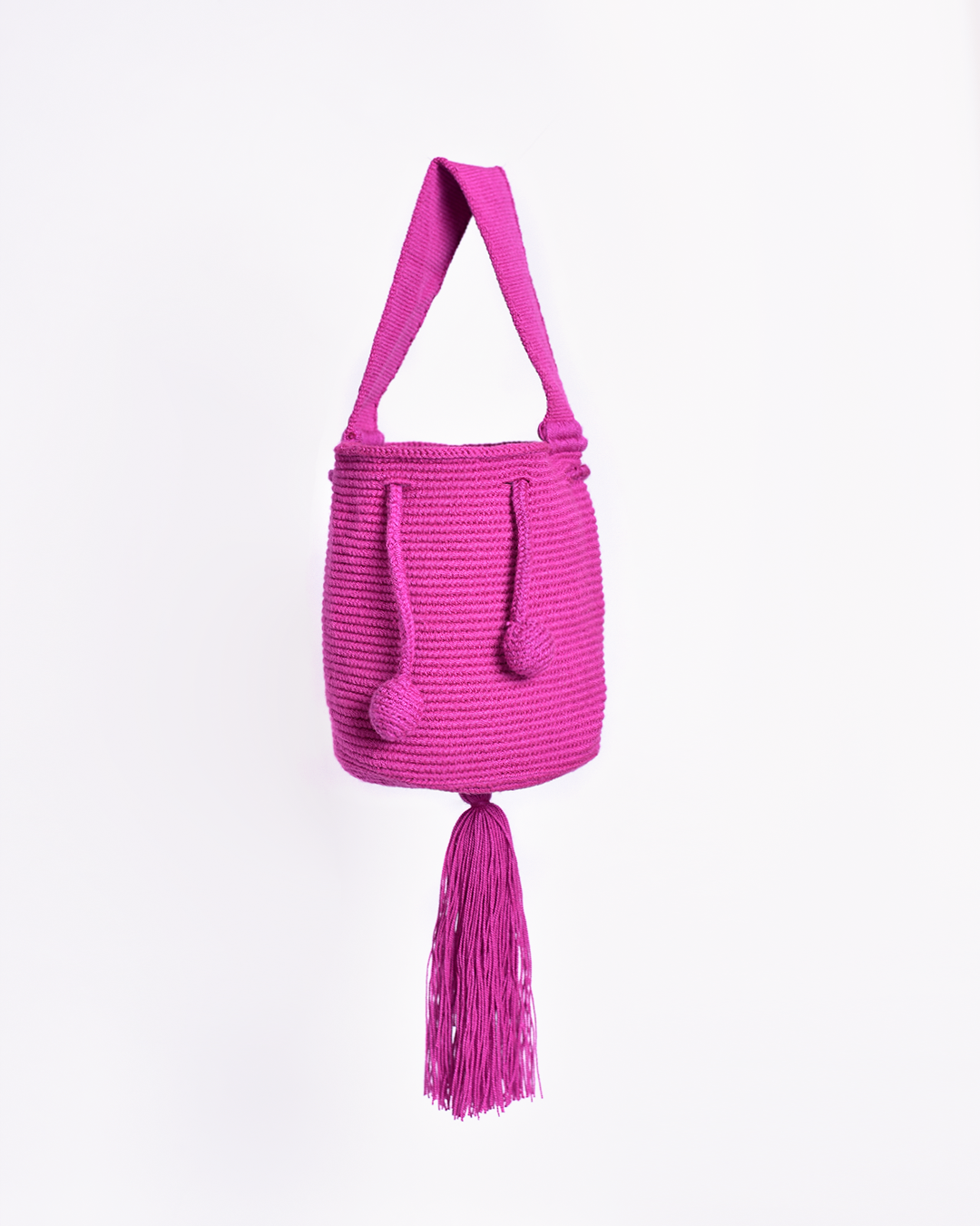 Mini mochila Wayuu artesanal, tejida a mano con hilo unicolor fucsia, con un colgante decorativo. Cuenta con una cargadera corta y un cordón ajustable. Hecha por artesanas de la comunidad Wayuu, reflejando la autenticidad de la moda colombiana.