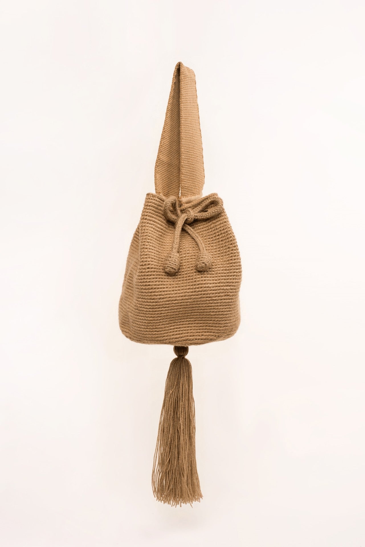 Mini mochila Wayuu artesanal, tejida a mano con hilo unicolor caqui, con un colgante decorativo. Cuenta con una cargadera corta y un cordón ajustable. Hecha por artesanas de la comunidad Wayuu, reflejando la autenticidad de la moda colombiana.