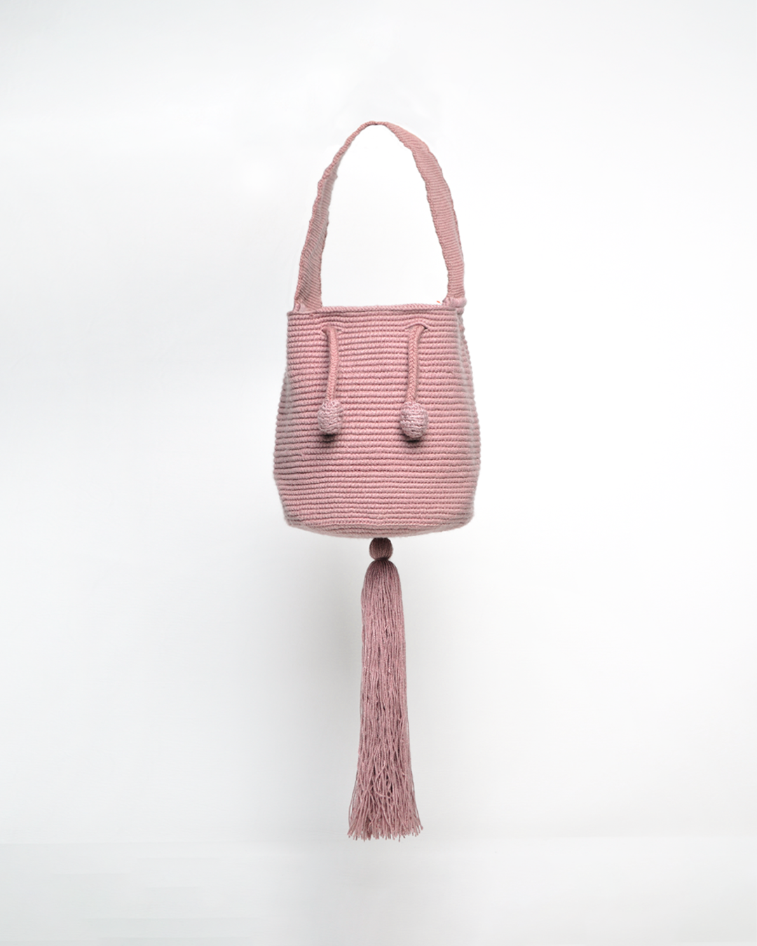 Mini mochila Wayuu artesanal, tejida a mano con hilo unicolor palo rosa, con un colgante decorativo. Cuenta con una cargadera corta y un cordón ajustable. Hecha por artesanas de la comunidad Wayuu, reflejando la autenticidad de la moda colombiana.