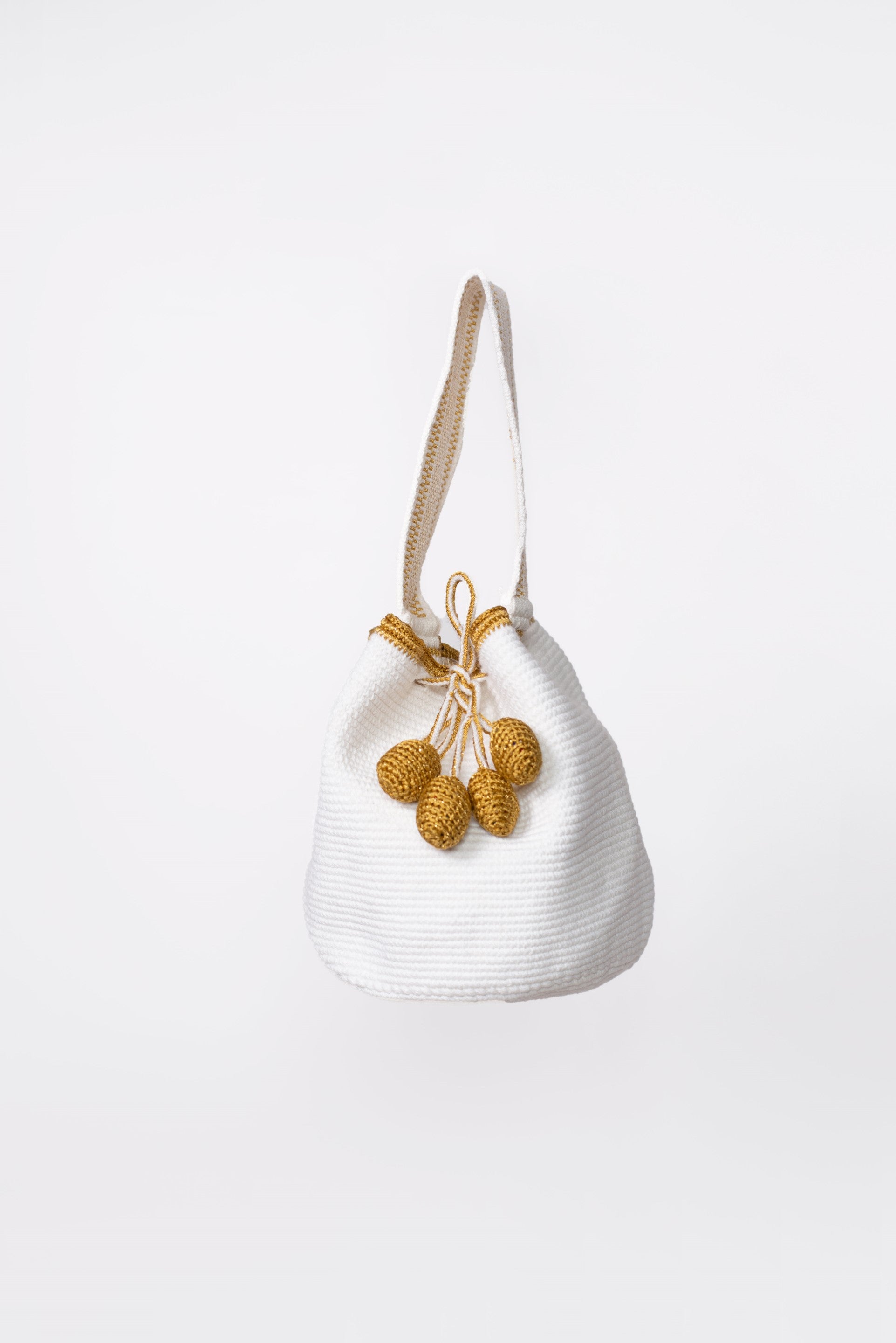 Mochila artesanal Wayuu en color blanco con detalles en hilo dorado. Tejida a mano con la técnica tradicional, cuenta con dos borlas y un asa corta. Ideal para quienes buscan un accesorio único y auténtico de moda colombiana.