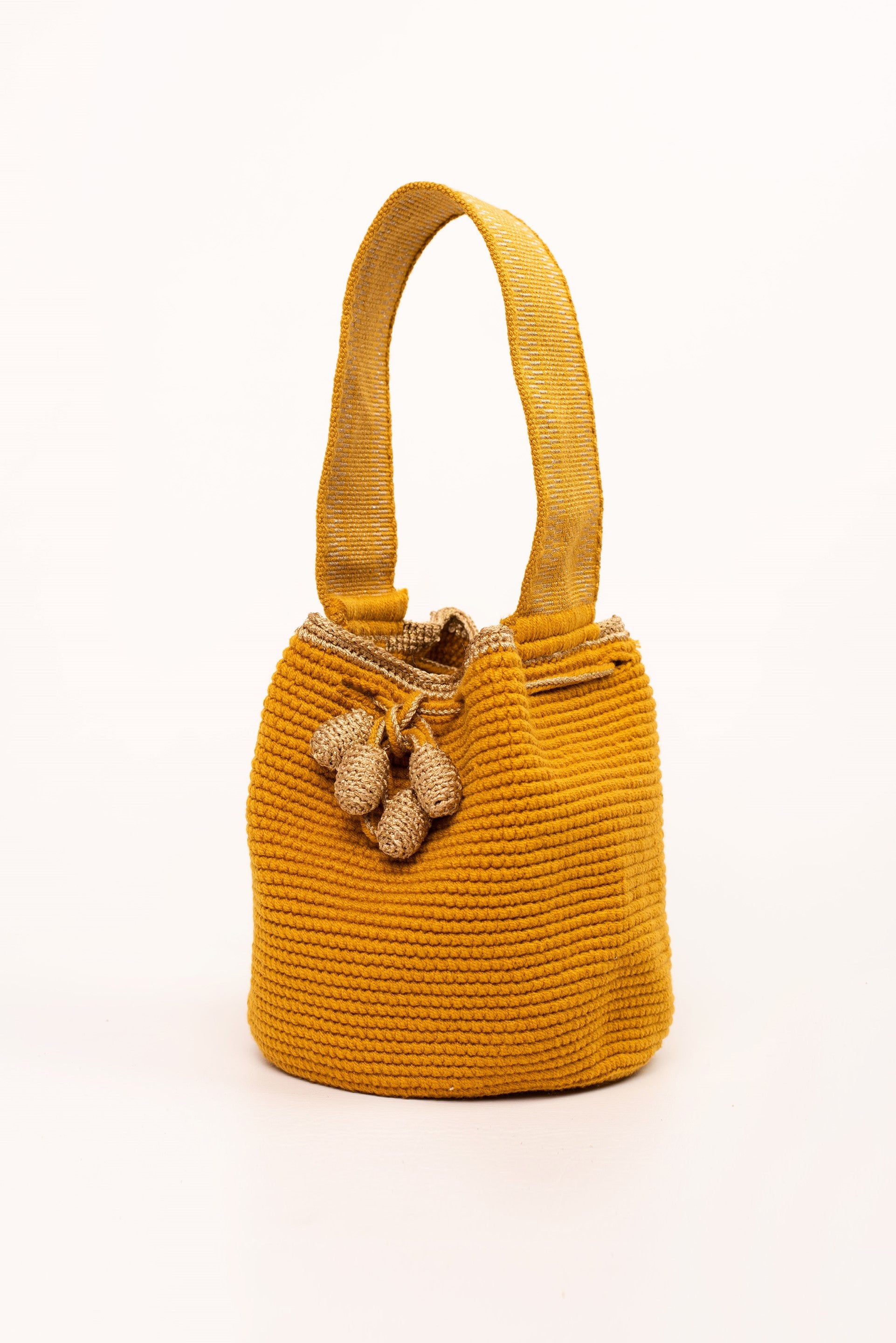Mochila artesanal Wayuu en color mostaza con detalles en hilo dorado. Tejida a mano con la técnica tradicional, cuenta con dos borlas y un asa corta. Ideal para quienes buscan un accesorio único y auténtico de moda colombiana.