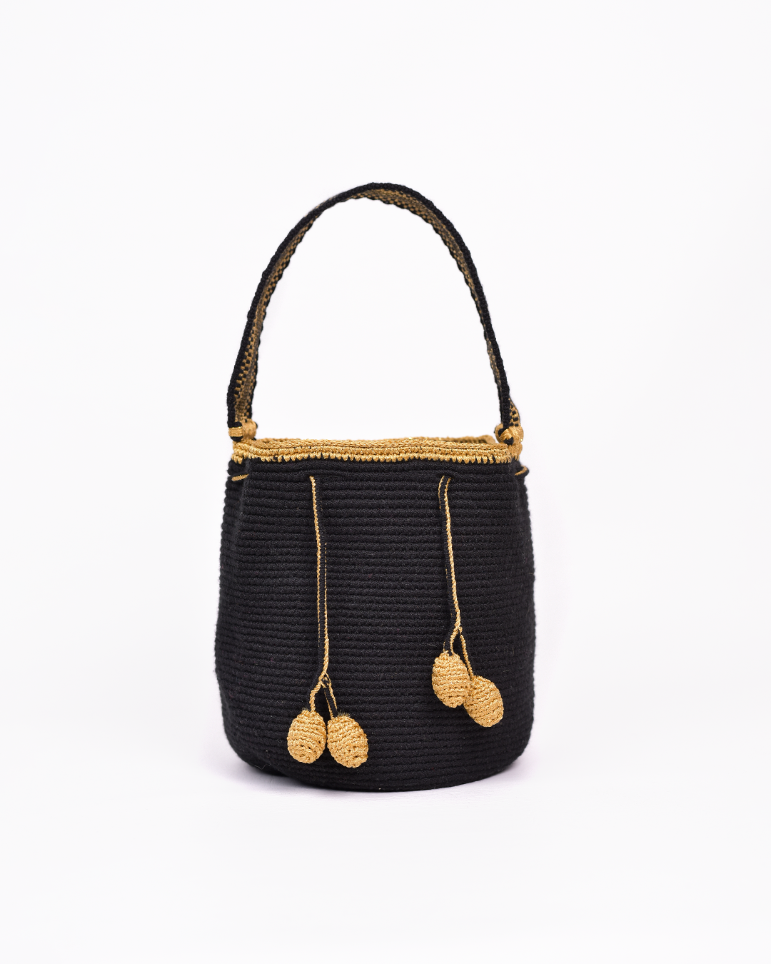 Mochila artesanal Wayuu en color negro con detalles en hilo dorado. Tejida a mano con la técnica tradicional, cuenta con dos borlas y un asa corta. Ideal para quienes buscan un accesorio único y auténtico de moda colombiana.