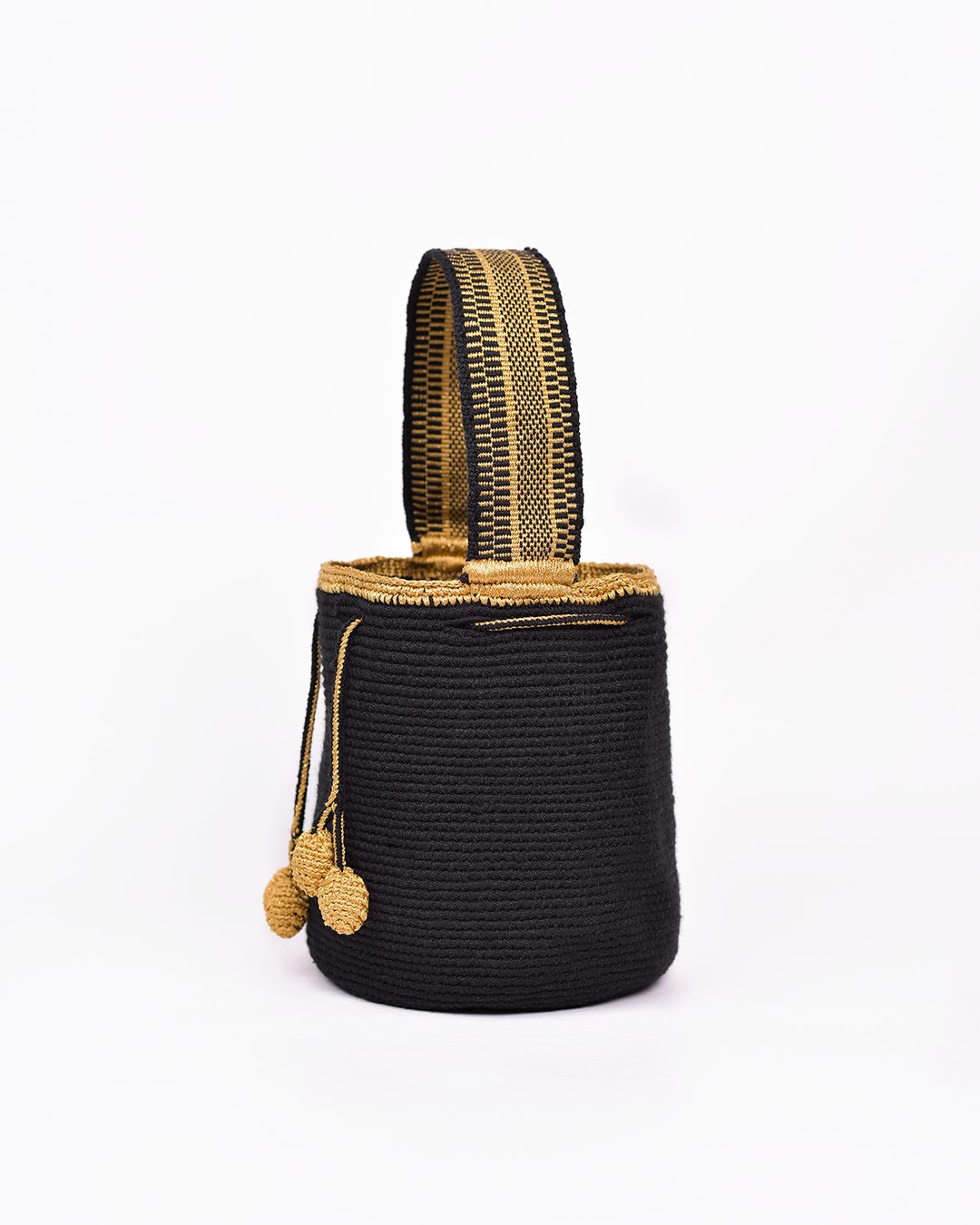 Mochila artesanal Wayuu en color negro con detalles en hilo dorado. Tejida a mano con la técnica tradicional, cuenta con dos borlas y un asa corta. Ideal para quienes buscan un accesorio único y auténtico de moda colombiana.