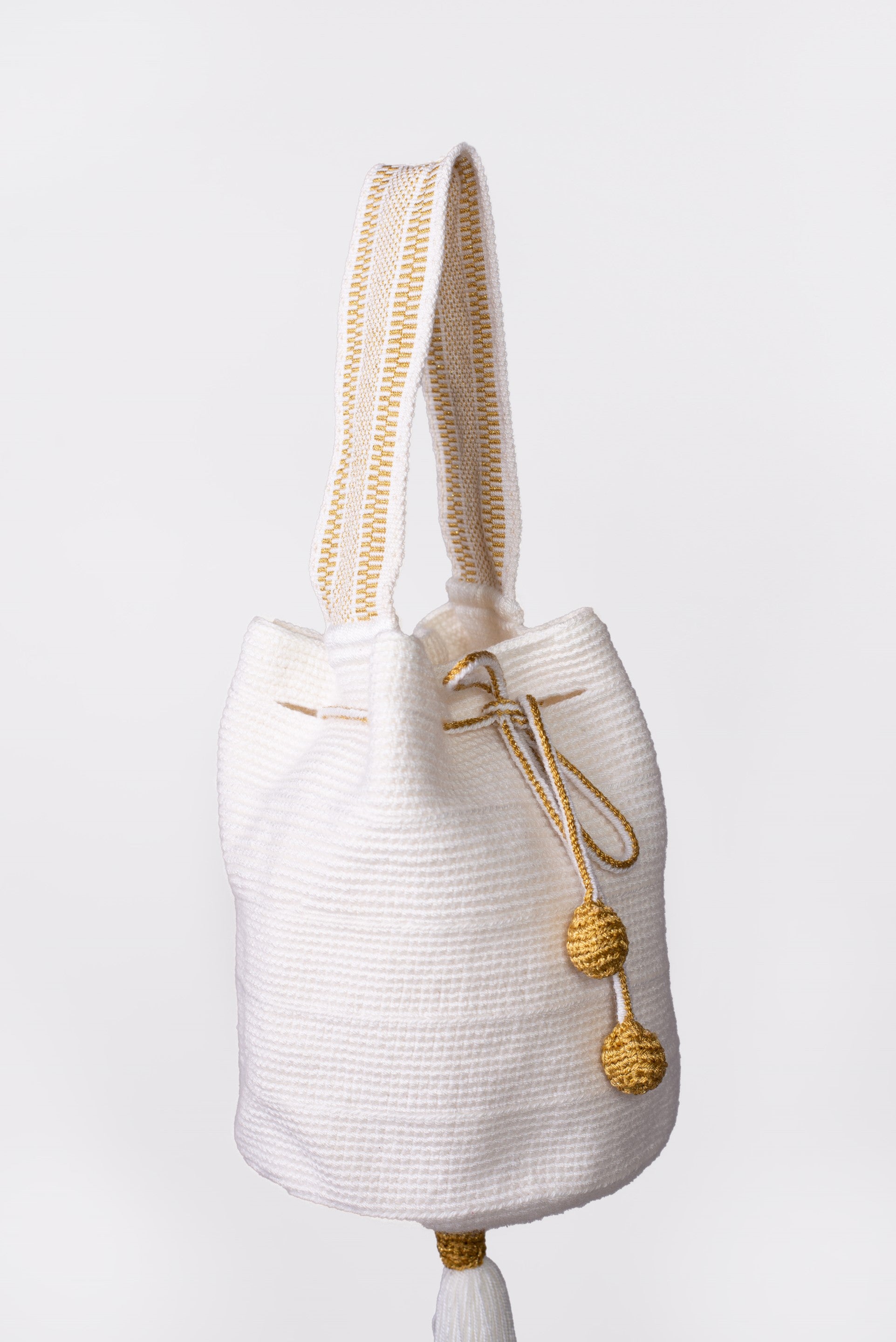 Mochila artesanal Wayuu de color blanco, tejida a mano con hilos de algodón y detalles de hilos dorados. Diseño con borlas decorativas y cordón ajustable. Ideal para quienes buscan moda colombiana única y auténtica. ¡Compra online en Micerino!