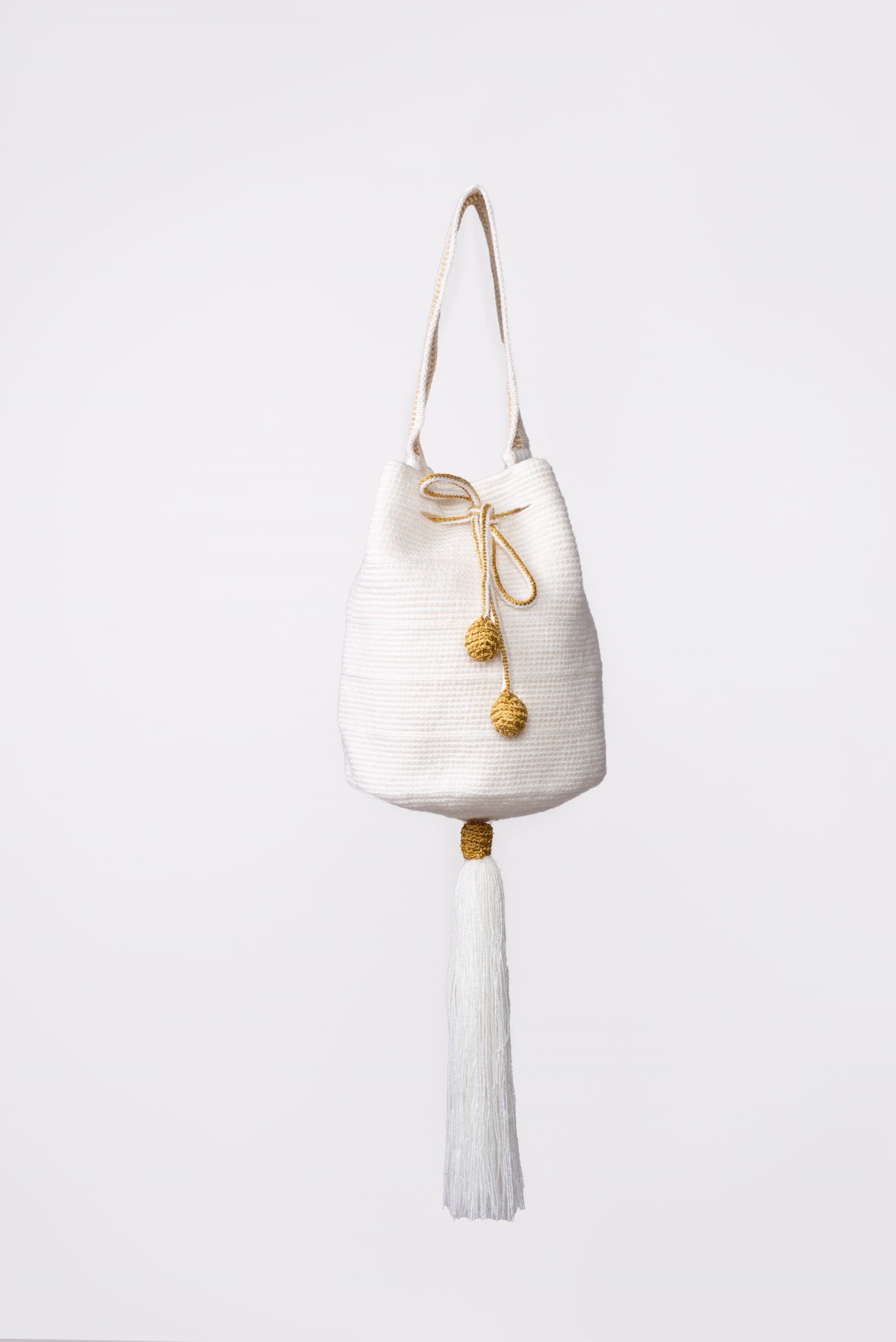 Mochila artesanal Wayuu de color blanco, tejida a mano con hilos de algodón y detalles de hilos dorados. Diseño con borlas decorativas y cordón ajustable. Ideal para quienes buscan moda colombiana única y auténtica. ¡Compra online en Micerino!