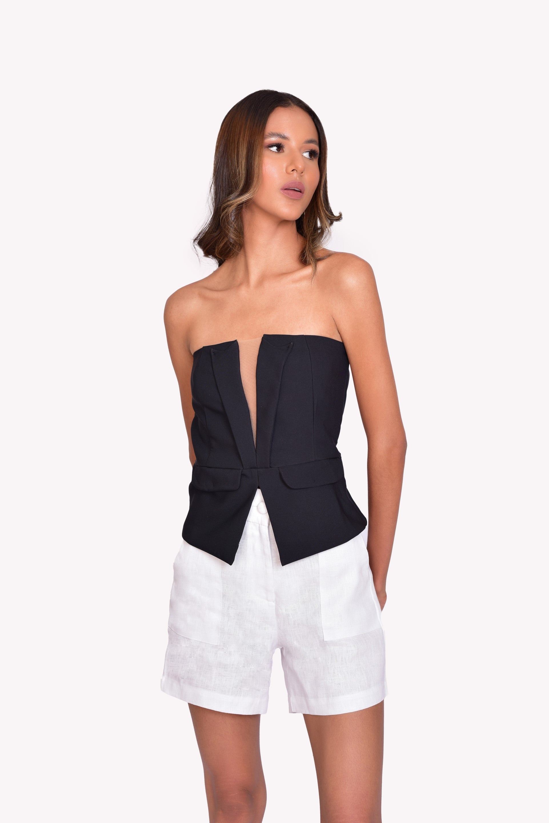 Top strapless negro con escote profundo y abertura frontal en diseño estructurado. Detalles de solapa que aportan sofisticación y elegancia. Perfecto para looks modernos y vanguardistas. ¡Compra online en Micerino!