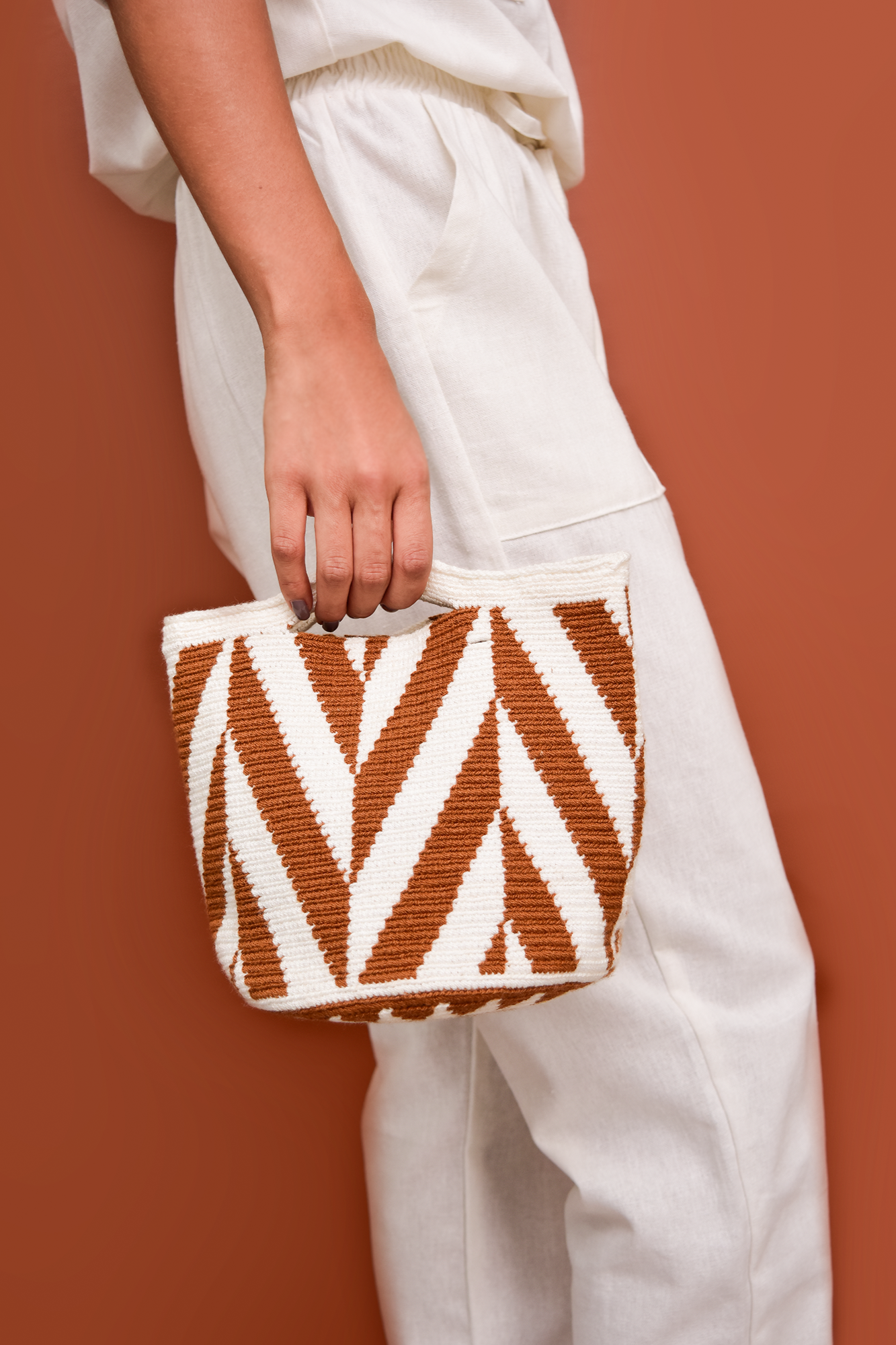 Bolso artesanal tejido a mano en tonos blanco y terracota, con un diseño geométrico de líneas en zigzag. Un accesorio versátil y auténtico, ideal para complementar cualquier look con un toque de estilo colombiano.