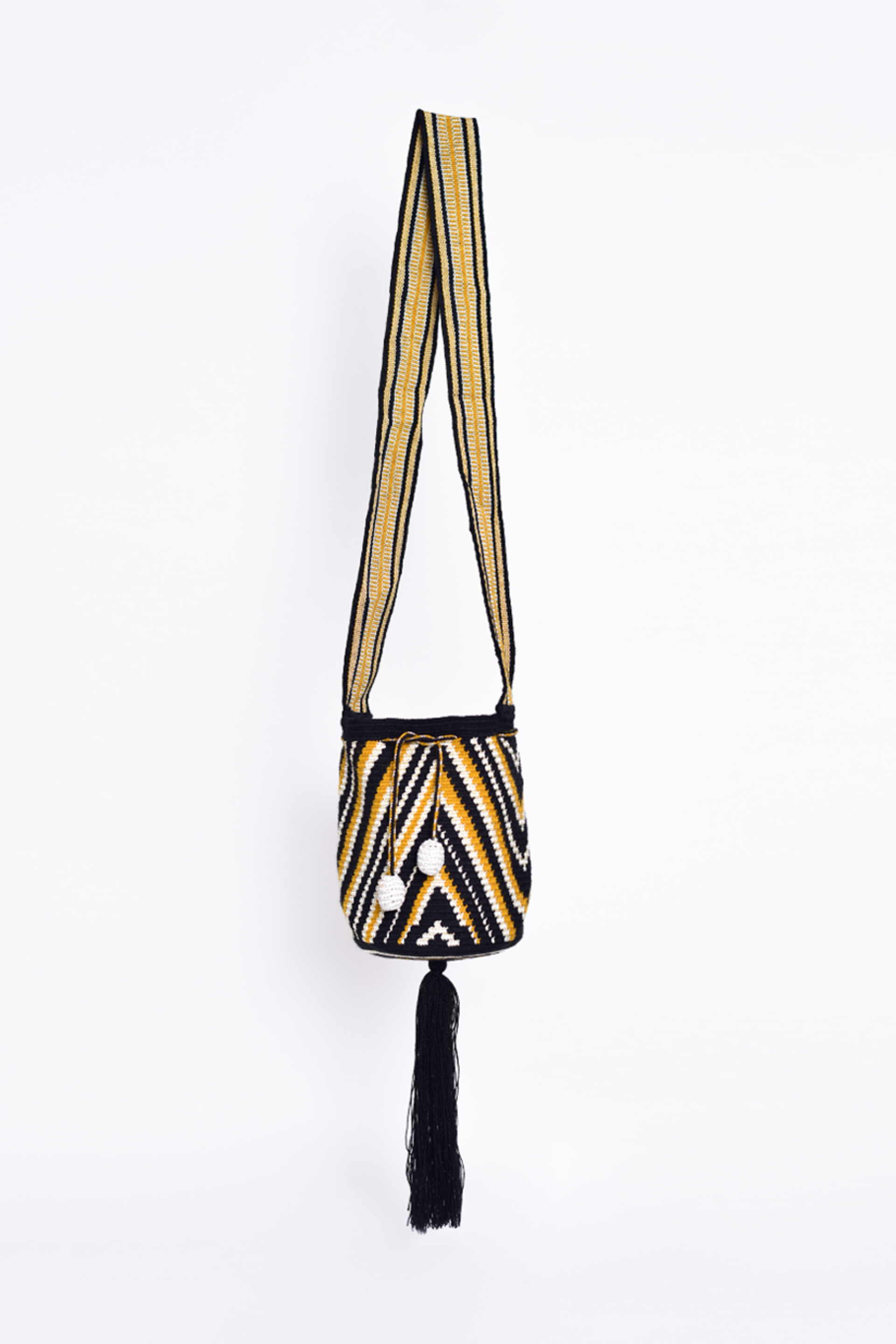 Mochila artesanal Wayuu con diseño geométrico en tonos negro, amarillo y blanco, detalles en los costados con pompones blancos y un fleco largo en la parte inferior.