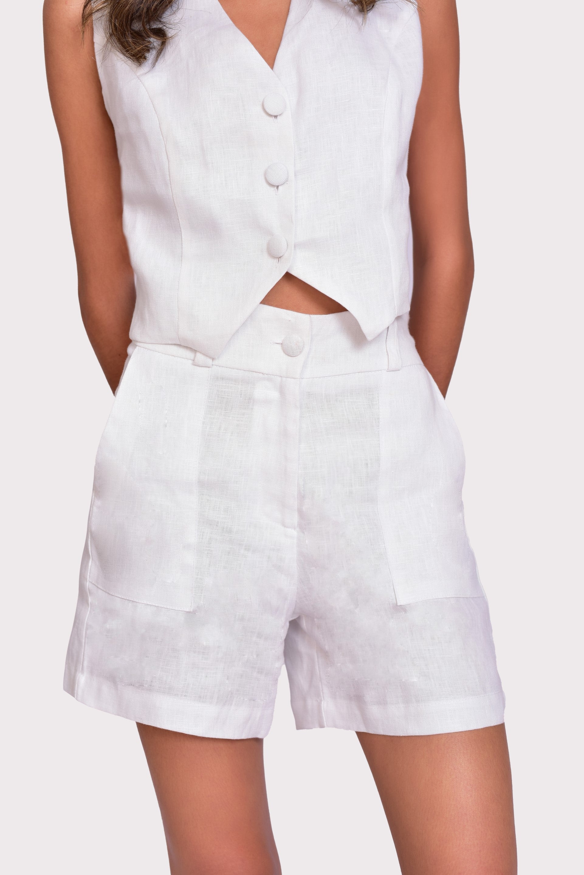 Conjunto blanco de lino, compuesto por top sin mangas y shorts. Ideal para un look fresco y elegante de verano, acompañado de un bolso negro de malla. Confeccionado en Colombia, perfecto para disfrutar de la moda colombiana con estilo.